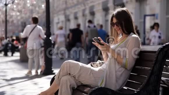 一个年轻的女孩坐在街上的长凳上背景是美丽的珠宝和版画在你的身上写了一条信息视频的预览图