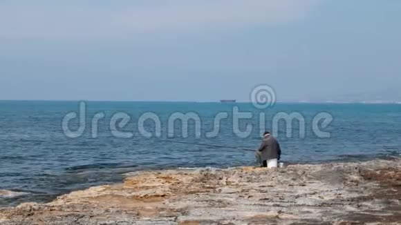 一个孤独的老人坐在空海滩上拿着投饵棒和钓鱼孤独的渔夫在海滩上视频的预览图