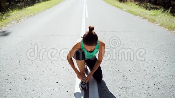 一个在森林沥青路上的女孩在运动鞋上系着花边慢动作视频的预览图