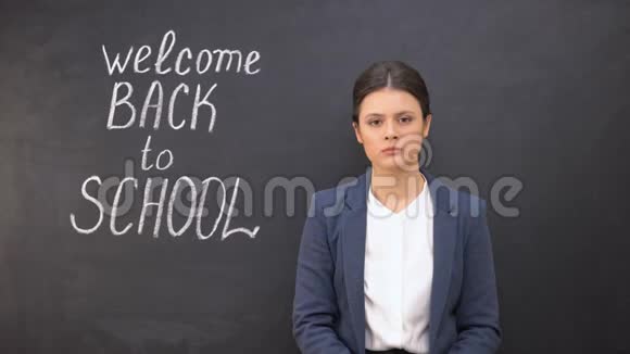 紧张的老师看着摄像机站在黑板附近欢迎回到学校视频的预览图