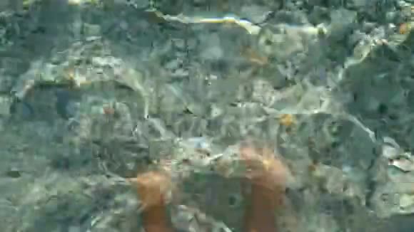 特写镜头人的腿在水里在爱琴海清澈的海水下可以看到多种颜色的小卵石视频的预览图