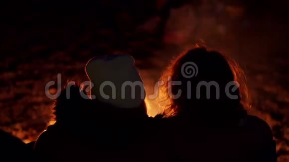 一对年轻夫妇坐在火炉旁在海边用帐篷露营两个视频的序列手持设备的背面视图视频的预览图