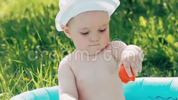 快乐的小男孩在草坪上的充气游泳池里玩玩具视频的预览图