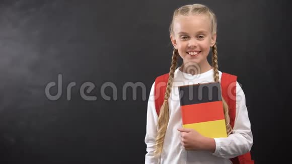 手持德语课本黑板背景的微笑女学生视频的预览图