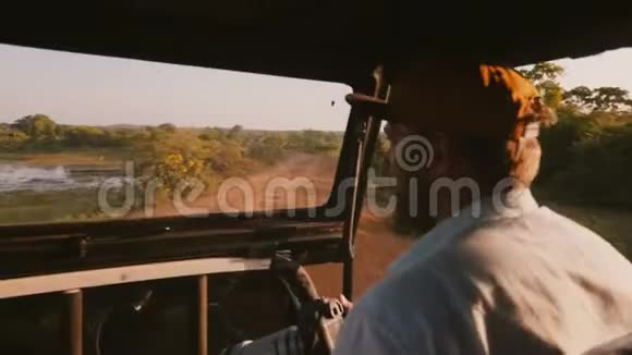 年轻快乐专注的男记者带着专业的相机在日落乘坐狩猎旅行汽车旅行热带视频的预览图