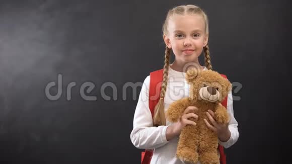 女孩子抱着背包玩具熊对着黑板对着镜头微笑视频的预览图