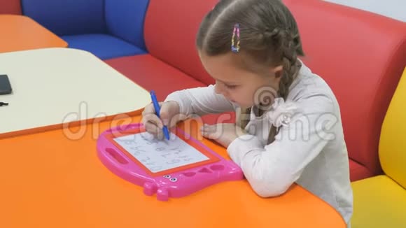 孩子们游戏室可爱的小女孩在磁性黑板上画特别的笔视频的预览图