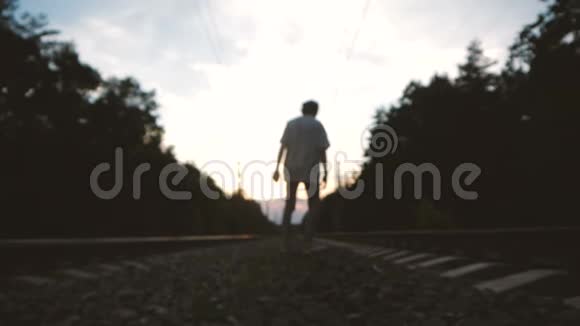 日落时分一个年轻的离群索居的家伙走在铁路轨道的中央视频的预览图