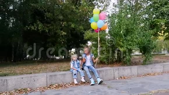 两个小女孩姐妹一个十几岁的女孩和一个小女孩坐在公园的长凳上有一大堆五颜六色的东西视频的预览图