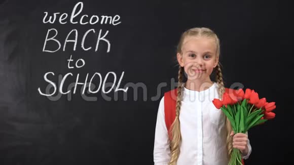可爱的微笑女孩拿着一束郁金香靠近黑板欢迎回到学校视频的预览图