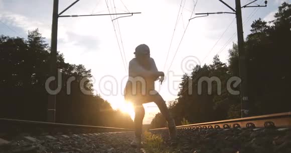 4k戴帽子的人在日落时分在铁轨旁的大自然上跳舞动作缓慢视频的预览图