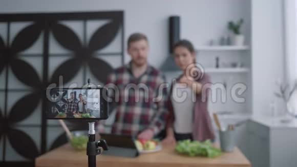 营养博客vloggers男女在厨房准备健康的早餐蔬菜和蔬菜同时拍照视频的预览图