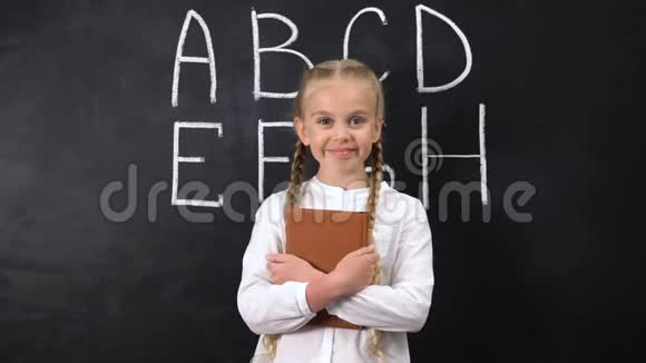 微笑女学生拥抱书后面黑板上写字母系统视频的预览图