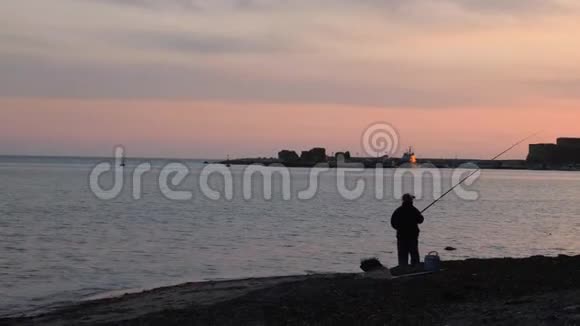 粉红色日落时人们在海上投掷鱼竿的剪影日落时分渔民在海滨捕鱼视频的预览图