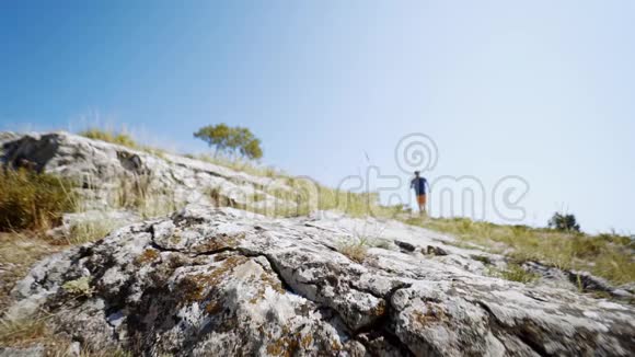 夏日迎着蓝天漫步在岩石坡上的年轻成年徒步旅行者视频的预览图