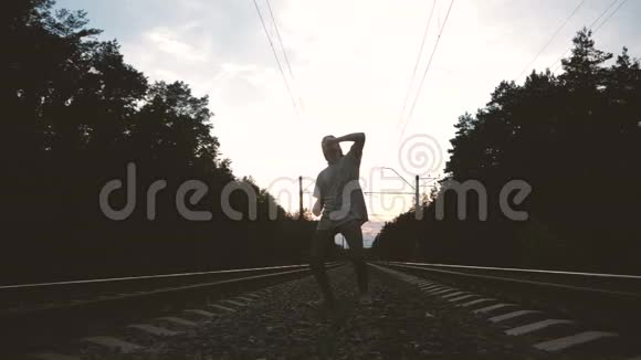 日落时分一个年轻人在铁轨附近跳舞动作缓慢视频的预览图