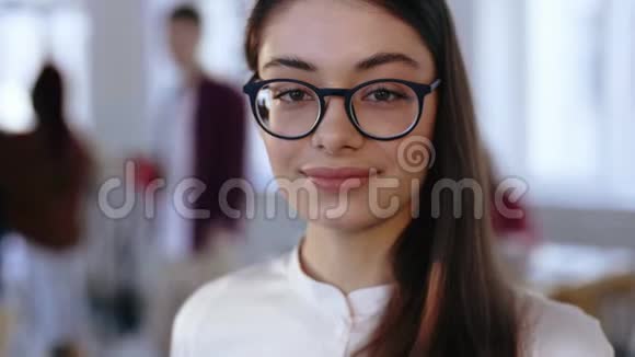 特写肖像快乐的年轻黑发设计专业商务女性戴着眼镜在办公室对着镜头微笑视频的预览图