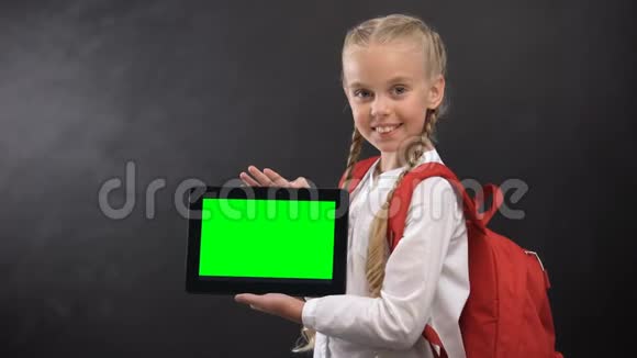 微笑的女学生展示平板电脑与绿色屏幕相机教育应用程序视频的预览图