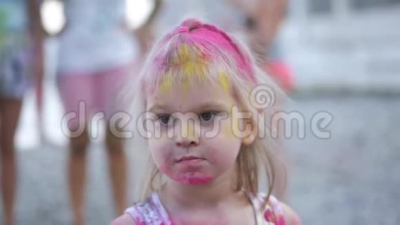 一个可爱的小女孩通过玩五颜六色的颜料和沙子来参加油漆节他的脸和衣服视频的预览图