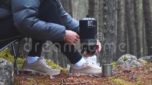 妇女使用燃气燃烧器在森林露营中温暖茶在徒步旅行中休息视频的预览图
