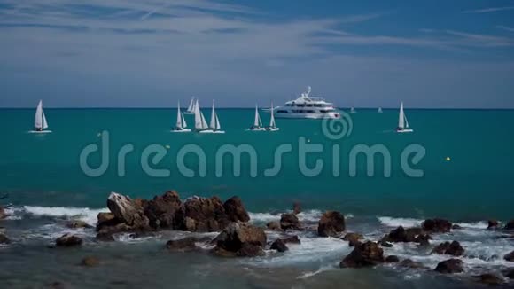 从岩石海岸的海面看帆船蔚蓝的海面上的白船色彩斑斓的背景视频的预览图