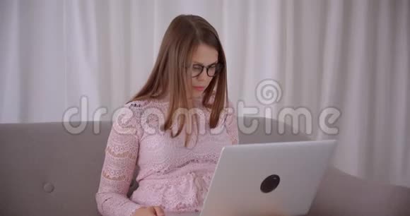 年轻有魅力的白种人女性在笔记本电脑上播放视频开心地坐在沙发上大笑视频的预览图