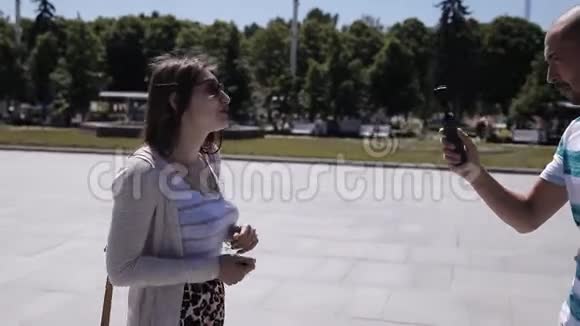 一个年轻人用摄像机拍摄一个女孩在城市的主要广场在欧洲广场记者报道视频的预览图