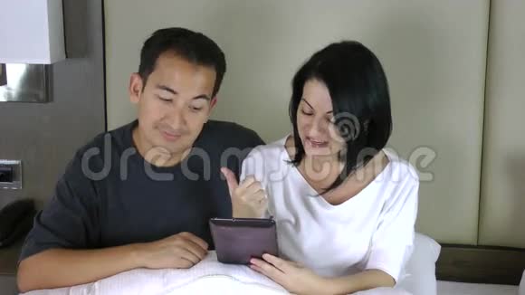 幸福的一对夫妇坐在床上看着平板电脑开了个会视频的预览图