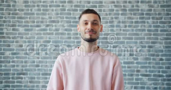 幸福的男人在砖墙背景上竖起大拇指微笑的肖像视频的预览图