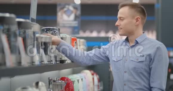 年轻漂亮的男人选择一个电水壶来买手里拿着一个设备研究价格标签和视频的预览图
