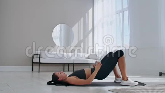 穿运动服的女人在做髋桥运动充满欢乐迷人的年轻女人躺在客厅的地板上做着时髦的动作视频的预览图