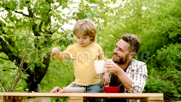 夏园晚会爸爸带儿子快乐的父亲和他的儿子坐在桌子上吃着健康的食物带着有趣的味道视频的预览图