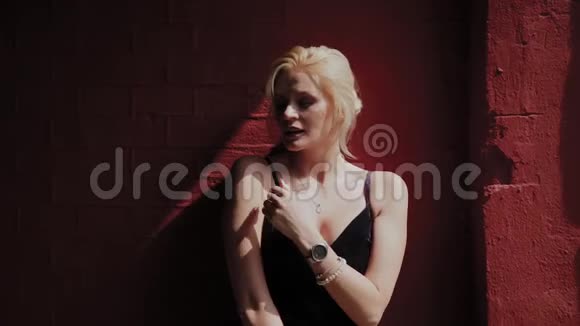 美丽而浪漫的女人站在红墙旁在严酷的阳光下视频的预览图