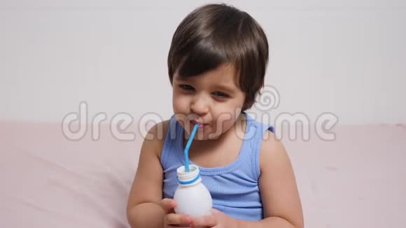 穿蓝色t恤的小男孩坐在家里的床上喝牛奶视频的预览图