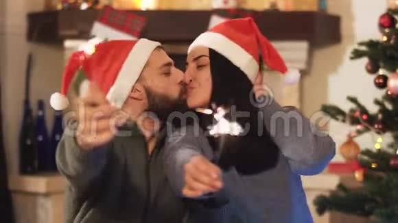 男人和女人坐在圣诞树附近女人手里拿着火花亲吻斯巴格勒燃烧前景视频的预览图