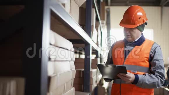 戴着头盔和工作服的负责任的工人站在架子旁边并在平板电脑上发布关于缺少工具的通知视频的预览图