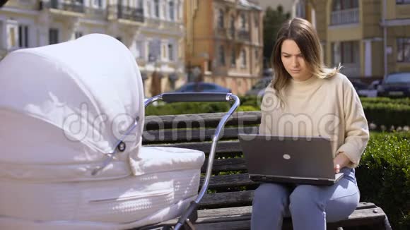 忙碌的年轻女性试图用手提电脑和婴儿车摆动新生儿儿童护理视频的预览图