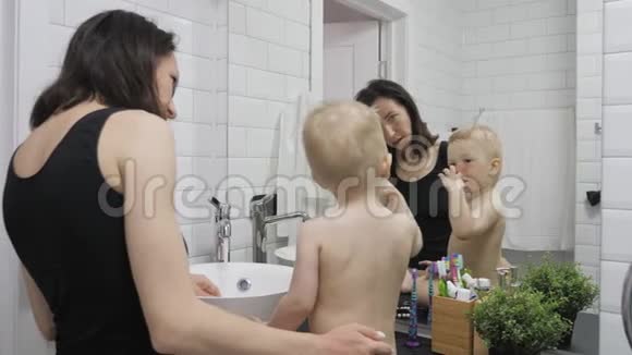 妈妈教孩子刷牙妈妈和孩子在刷牙时看镜子卫生概念视频的预览图
