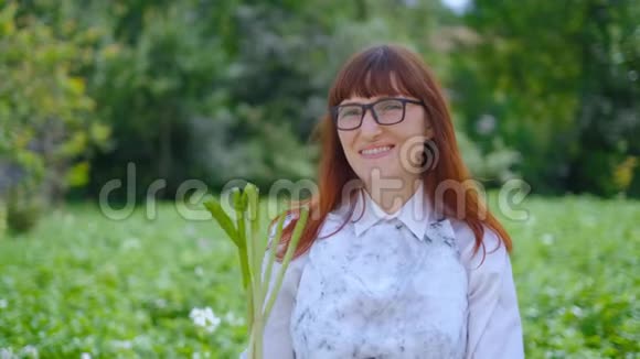 年轻的女农民在农场或花园里收获大蒜鳞茎手里拿着一堆蔬菜开心地笑着视频的预览图