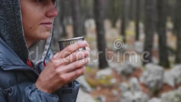 在森林里用金属杯喝茶的年轻女子徒步旅行者的特写镜头视频的预览图