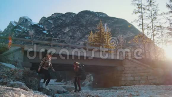 两个年轻的女人在山上的一座桥下的岩石河上视频的预览图