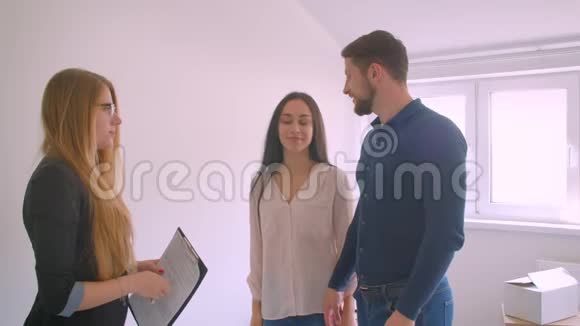 一对年轻的白种夫妇从他们的新公寓里得到钥匙房地产经纪人兴奋地接吻和拥抱视频的预览图