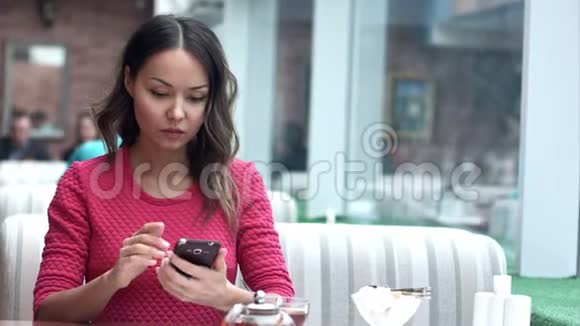 亚洲女人在咖啡馆里看手机喝茶视频的预览图