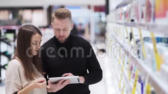 化妆品店里的年轻男女看着数码平板电脑说话视频的预览图