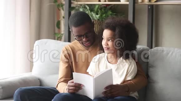 爱的黑人父亲拥抱孩子女儿在家读书视频的预览图