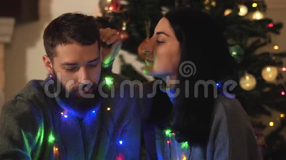 男人和女人坐在新年树附近脖子上戴着花环女孩抚摸她男朋友的头发胡须亲吻视频的预览图