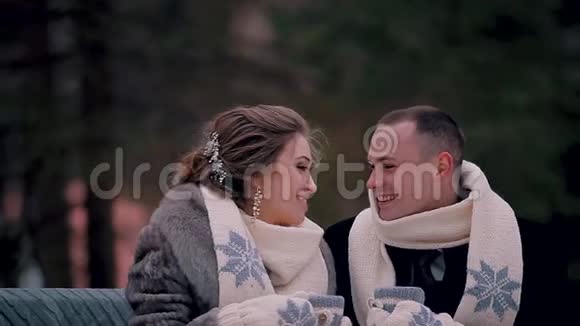 冬天情侣们坐在公园里的长凳上围着围巾手上戴着手套手里拿着热咖啡杯视频的预览图