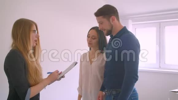 年轻的白种人夫妇与房地产经纪人签署文件并环顾他们的新公寓感到兴奋视频的预览图