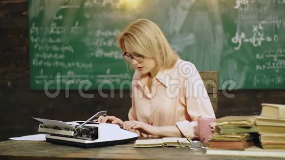 女人在桌子上用打字机打印文本在学校董事会的背景上有一堆书打字员视频的预览图
