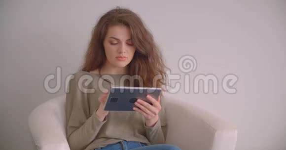 女商人在扶手椅上摆弄平板电脑固定地看着镜头在白色背景下忙碌地孤立着视频的预览图